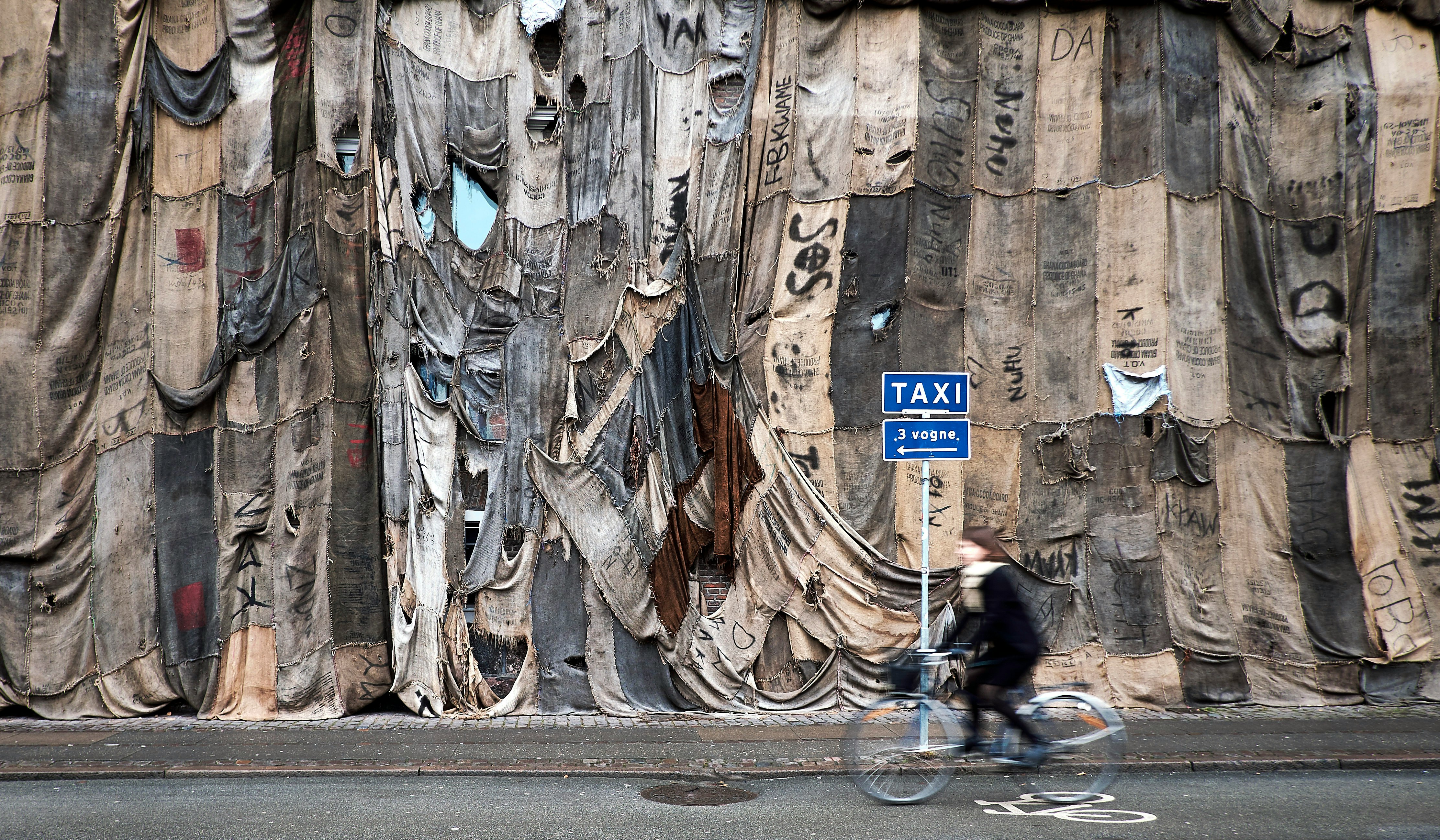 person riding bike on road beside cloth covered wall